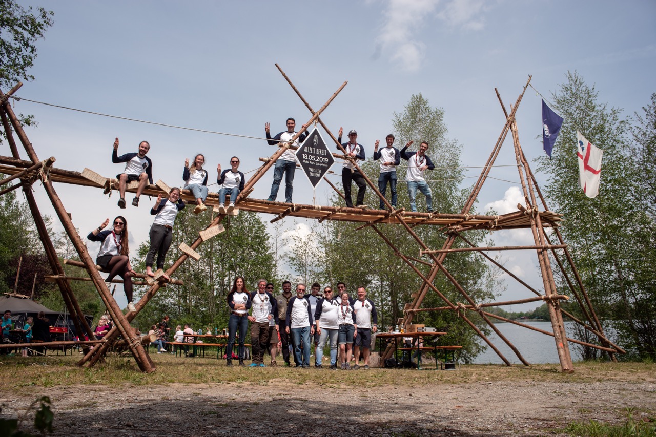 Pfadfindergruppe posiert auf hoher Lagerkonstruktion aus Holzstangen
